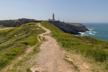 Santander, İspanya. Cabo Belediye Başkanı Deniz Feneri 'nin güneşli manzarası Biscay Körfezi' nin yukarısındaki uçurumlara tünemiş, kül taşı silindirik kuleyi saran kayalık sahil ve deniz manzarası