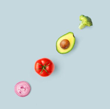 Mavi arka planda domates, avokado, soğan ve brokoliden yapılmış yaratıcı bir düzen. Düz yatıyordu. Yiyecek konsepti.
