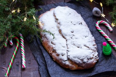 Christmas stollen with dried fruits, nuts and spices, Christmas decorations on a dark wooden background. Rustic style, selective focus.