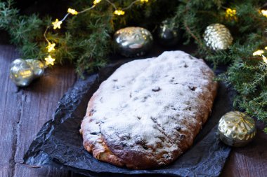 Christmas stollen with dried fruits, nuts and spices, Christmas decorations on a dark wooden background. Rustic style, selective focus.