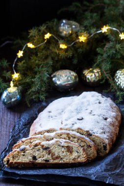 Christmas stollen with dried fruits, nuts and spices, Christmas decorations on a dark wooden background. Rustic style, selective focus.