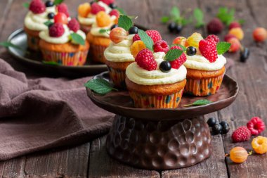 Tereyağlı kremalı ve ahudududulu kek, ahşap bir yüzeyde böğürtlenlerle süslenmiş. Kırsal biçim, seçici odak.