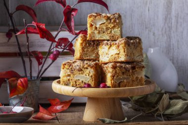 Slices of Dutch apple cake with streusel on a wooden tray, apples and apple branches on a wooden background. Rustic style, selective focus. clipart