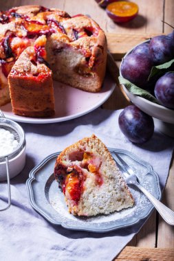 Doldurulmuş erik turtası ve şeker hamuru. Tahta bir masanın üzerine pudra şekeri ve erik serpiştirilmiş. Sonbahar durgun hayat, köy tarzı, seçici odaklanma.
