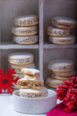 Alfajor, dolce de leche ile dolu kısa hamurlu pastadan yapılan geleneksel bir Latin Amerika kurabiyesi. Hafif bir arka planda Alfajores ve Noel dekoru.