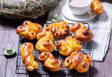 Traditional saffron Swedish buns lussekatt in different shapes, served with cocoa on a wooden table. Buns for St. Lucias Day. Rustic style, selective focus. clipart