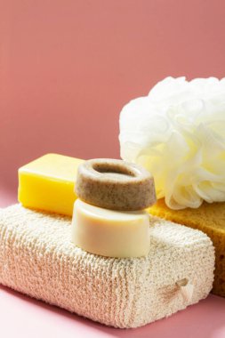 Banyo aksesuarları, farklı boyutlarda ve şekillerde süngerler ve pembe arka planda el yapımı sabunlar. Cilt bakımı için birey seti.