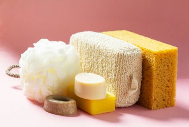Banyo aksesuarları, farklı boyutlarda ve şekillerde süngerler ve pembe arka planda el yapımı sabunlar. Cilt bakımı için birey seti.