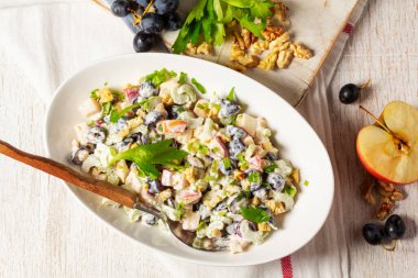 Elmalı, kerevizli, üzümlü ve cevizli mayonez salatası maydanozlu. Geleneksel Amerikan salatası, hafif arka planda meyveler ve fındıklar, seçici odaklanma.