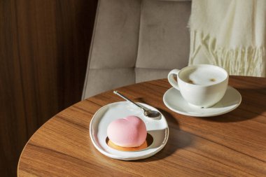 Pembe kadifeyle kaplanmış kalp şeklinde kremalı pasta ve bir kafedeki masada bir fincan latte. Tatlı, içki, bir kafede ahşap masa, seçici bir odak..