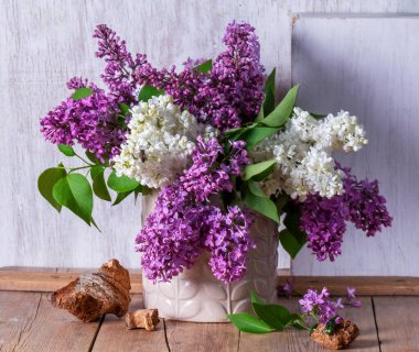 Açık arkaplanda bir buket leylak, odun parçaları ve böcekler. Bahar aylarında ahşap bir masanın üzerindeki leylak buketi gibi, kırsal tarzda, seçici bir odak noktası..