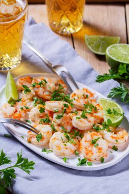 Sarımsak ve otla pişirilmiş karides, ahşap bir masada bira ve limonla servis edilmiş. Kırsal biçim, seçici odak.