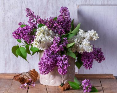 Açık arkaplanda bir buket leylak, odun parçaları ve böcekler. Bahar aylarında ahşap bir masanın üzerindeki leylak buketi gibi, kırsal tarzda, seçici bir odak noktası..