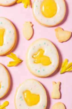 Limonlu, turuncu kremalı Paskalya yumurtası kurabiyeleri, pembe arka planda beyaz krema ve fındıklı çiçeklerle kaplı. Seçici odak.