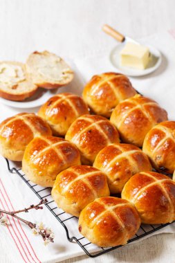 Tereyağı ve çiçek açan kayısı dallarıyla servis edilen sıcak haç çörekleri. Geleneksel İngiliz Paskalya çörekleri metal bir rafta, tereyağı ve havlu hafif bir masada, köy tarzı..