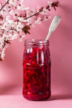 Pancar, biberiye, hardal ve diğer baharatlarla birlikte salamura lahana ve erik çiçeği. Lahana turşulu cam kavanoz, pembe arka planda çiçek açan erik dalları. Seçici odak.