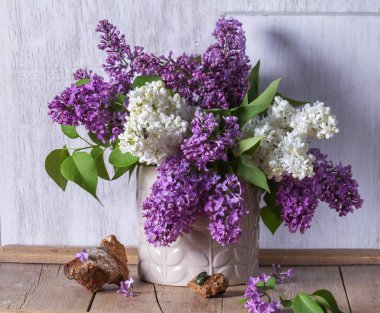 Açık arkaplanda bir buket leylak, odun parçaları ve böcekler. Bahar aylarında ahşap bir masanın üzerindeki leylak buketi gibi, kırsal tarzda, seçici bir odak noktası..