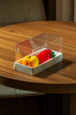 Kutuda meyve ve böğürtlen şeklinde bir kremalı pasta seti. Üzerinde şeftali şeklinde pastalar ve bir kafedeki masada çilek olan karton kutu, seçici bir odak.