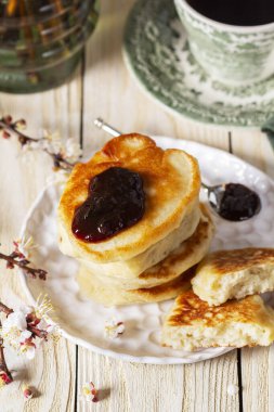 Erik reçeli ve çaylı maya krepleri ve hafif ahşap bir masada bir buket çiçekli kayısı dalları. Kırsal biçim, seçici odak.