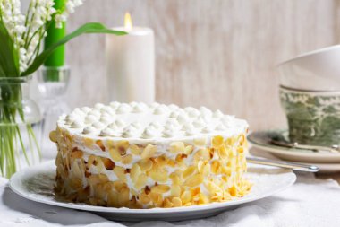 Badem yaprakları ve mumlarla süslenmiş ince katmanlardan yapılmış ekşi krema ve ballı pasta. Kutlama pastası, bir fincan nane çayı, bir buket vadi zambağı ve arka planda mumlar. Kırsal biçim.