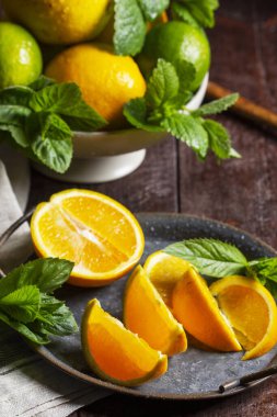 Portakallar, limonlar, limonlar, nane ve limon merhemi ve ahşap zemin üzerinde güneş tarafından aydınlatılmış yağmur damlaları. İçecek, çay ya da limonata yapmak için turunçgiller ve otlar.