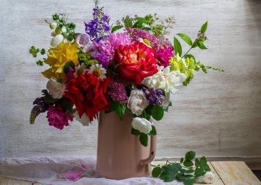 A bouquet of different flowers, roses, peonies, lupines, daisies, dilphinium, snapdragon and others in an old teapot. Rustic style.