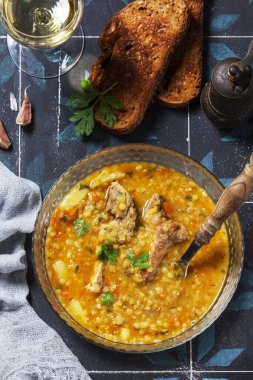 Lentil soup with pork and vegetables, served with white wine and croutons. High-protein, healthy soup. Rustic style, selective focus.