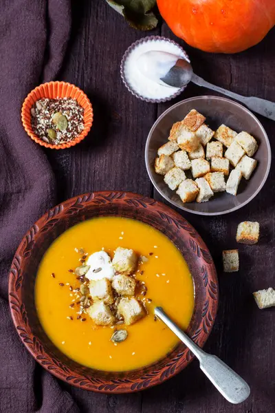 Kabak kremalı çorba, kızarmış ekmek, krema ve tohumla servis edilir. Koyu bir ahşap masada sonbahar sebze çorbası. Kırsal biçim, seçici odak.