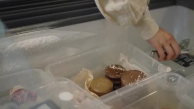 Woman takes fresh bakery with metal utensil pastry tongs putting into paper box. Female customer buys delicious dessert in supermarket closeup