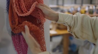 Woman chooses ecological mesh bag for products on blurred background in shop. Female customer enjoys buying useful things in supermarket closeup