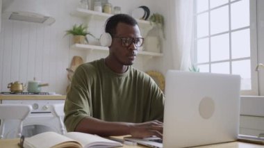 African American male web developer or programmer working at home behind a laptop. Freelancer working online in headphones, working on a new project.