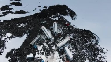 Flight around the hotel in barrels on the slopes of Elbrus in the highlands in the rocks and snow on the glacier, aerial view. Extreme hotel in the highlands for climbers climbing to the top.