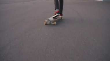 Man jumps on skateboard riding on asphalt sports ground in city under cloudy sky. Active guy enjoys making tricks on board at sunset closeup. Russia, St. Petersburg, August 2022