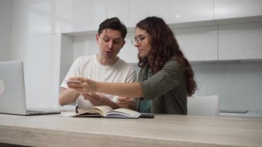 Young husband and wife discuss money sums in supermarket check and argue about expenses at table with laptop and calculator in kitchen