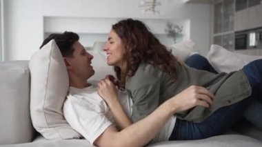 Young couple in love lies on the sofa and kisses, tickles each other and has fun together on a bright day at home