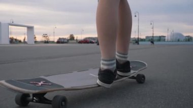 Young man stands on skateboard kicking off asphalt road on city street at sunset. Active guy enjoys riding board in evening closeup slow motion