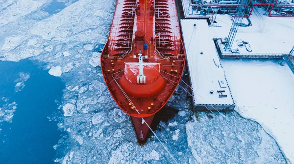 冷たい冬の空中ビューで壊れた氷の厚い層で覆われた水のターミナルポンプシステムから大きな赤いタンカーに石油出荷 — ストック写真