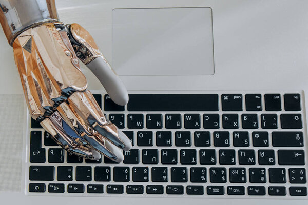 Young woman uses modern metal bionic arm to type on laptop keyboard sitting at wooden table in light room extreme close view