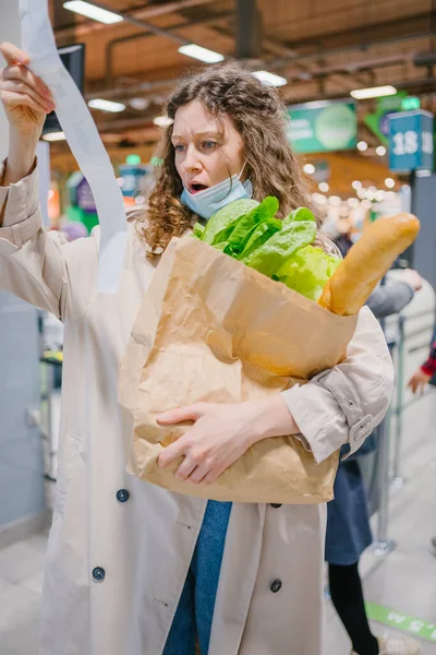 여자는 식료품 가게에서 수표를 들여다보고 쇼핑백을 불쾌하게 치솟는 — 스톡 사진