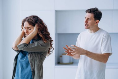 Curly-haired woman plugs ears in stress not wanting to hear angry husband quarrel shout and argue about family problems closeup
