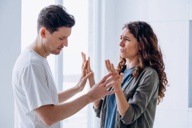 Married curly-haired woman quarrels angrily gesticulating and shouting with brunet husband over family problems standing in kitchen closeup