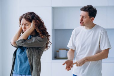 Curly-haired woman plugs ears in stress not wanting to hear angry husband quarrel shout and argue about family problems closeup