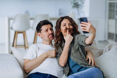 Gülümseyen esmer kadın ve kısa saçlı genç adam fotoğraf ve videolar için bıyık şeklinde kıvırcık saçlı poz veriyorlar.