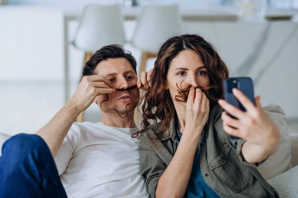 Gülümseyen esmer kadın ve kısa saçlı genç adam fotoğraf ve videolar için bıyık şeklinde kıvırcık saçlı poz veriyorlar.