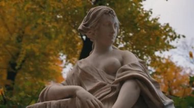 Circular movement of the camera around the sculpture of a woman in an autumn park in cloudy weather against the background of yellow trees.