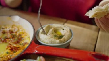 Woman spreading delicious hummus on a piece of bread tortilla with a fork in a sunny cafe, close-up hands