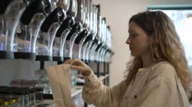Young woman with curly hair pours chickpeas into a paper craft bag in an eco-friendly unpackaged store. The concept of zero waste, care for the environment