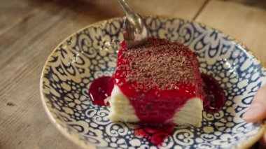 Woman with a small spoon breaks off a piece from an appetizing sweet cake poured with red syrup in a cafe close-up. Sweet tooth, sugar addiction.