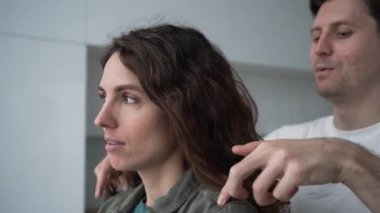 Young loving husband flirts with angry curly-haired wife standing by window after severe argument and woman forgives smiling closeup