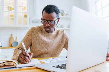 Genç Afrikalı Amerikalı adam internette çalışıyor. Masaya notlar yazıyor..